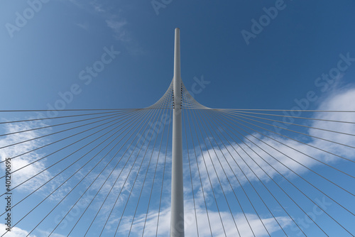 From below of white contemporary suspension bridge with high column connecting many cables together against blue sky