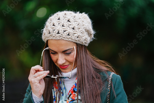 Calm female wearing knitted beret putting on trendy sunglasses during stroll in autumn park