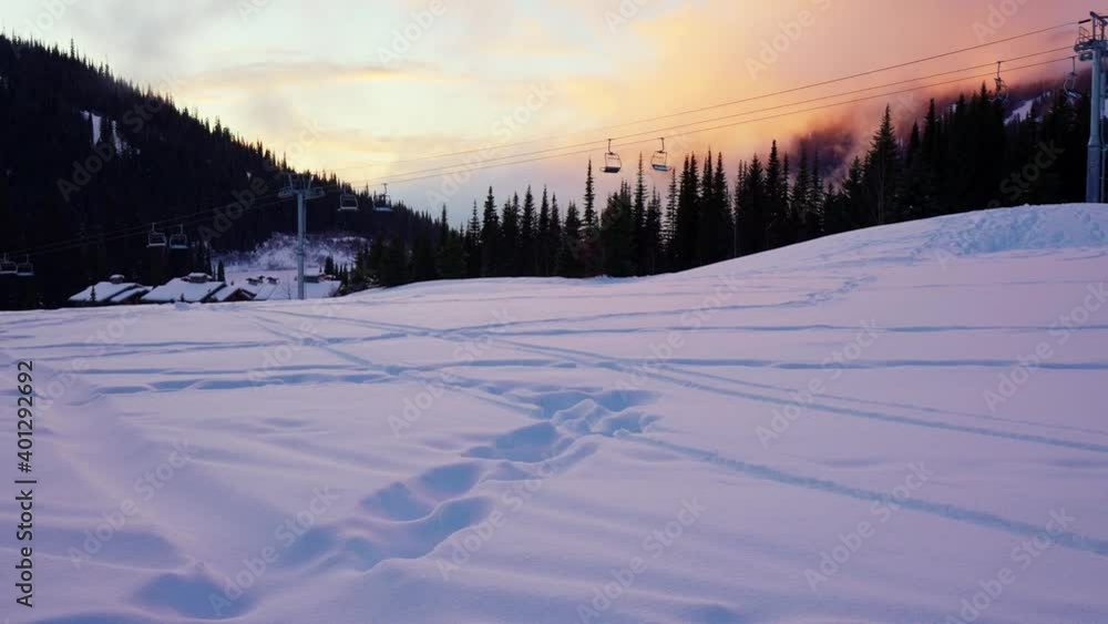 Empty moving cableway lift chairs on the snowy ground and trees at sunset Empty moving cableway lift chairs on the snowy ground and trees at sunset