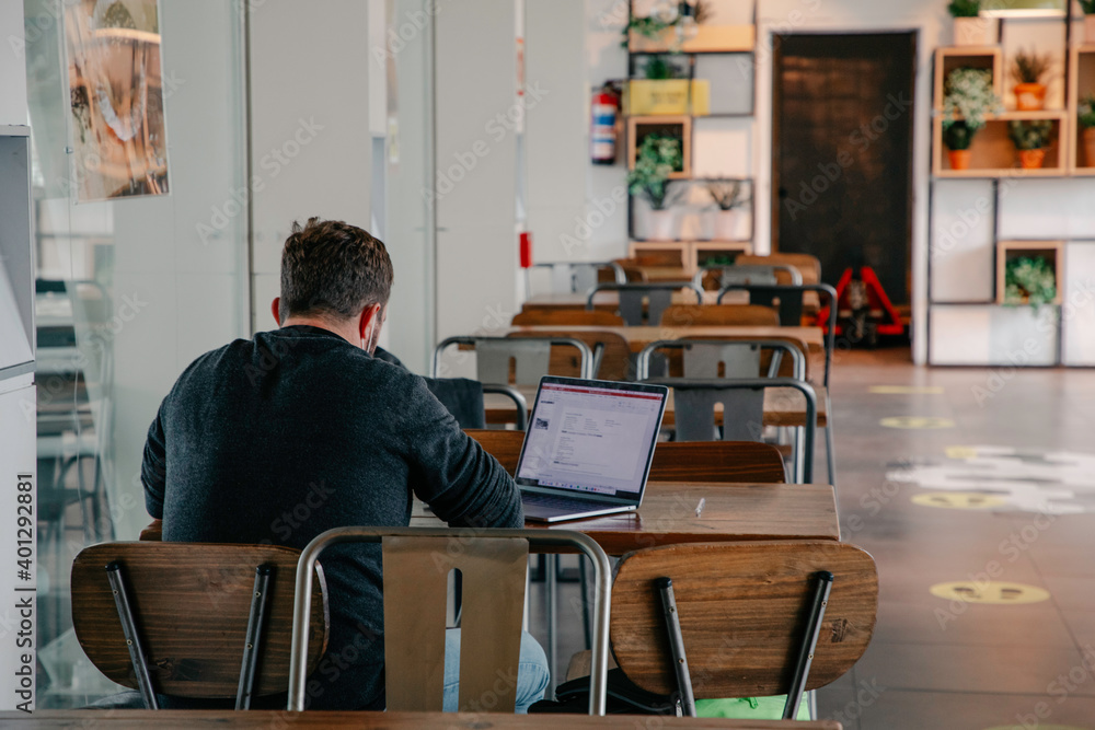 man sitting in a cafeteria with his back turned while working with his laptop