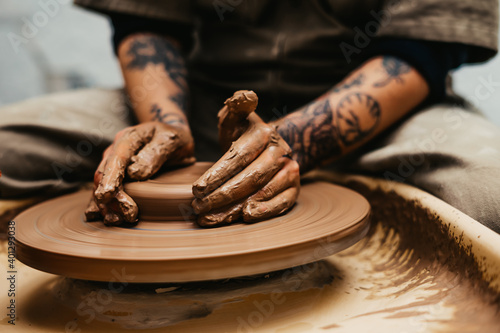 Closeup of dirty hands of anonymous craftsman using pottery wheel and making clay pot in workshop photo