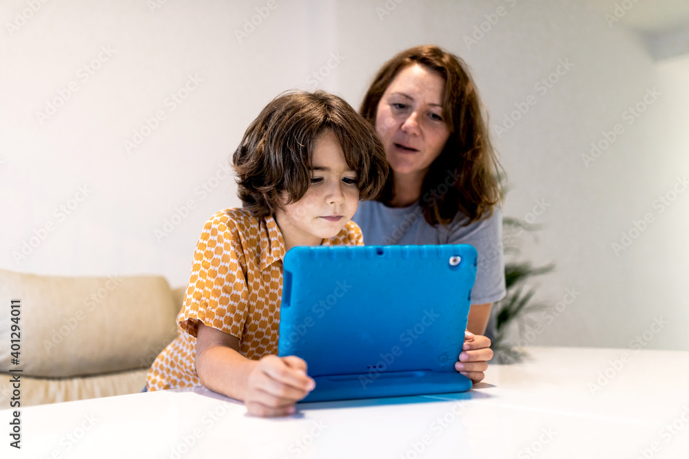 Kid with bright netbook at table near content mother in house Kid with bright netbook at table near content mother in house