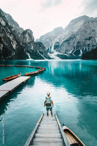 Back view of unrecognizable male traveler standing on wooden quay and admiring amazing scenery of lake with turquoise water in mountains on foggy day photo