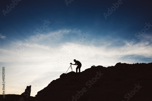 Silhouette Of A Photographer With A Tripod Against The Blue Sky With Clouds