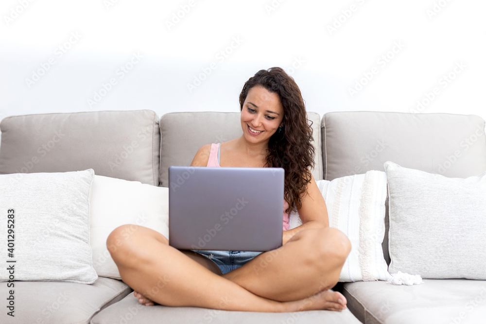 Cheerful young female in casual clothes sitting on comfortable couch and watching video on laptop while chilling at home Cheerful young female in casual clothes sitting on comfortable couch and watching video on laptop while chilling at home