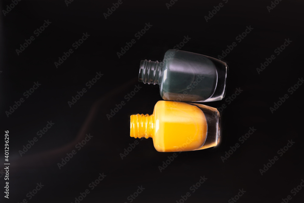 Two of multicolored bottles of nail polish with reflections in a mirror surface on a dark background Two of multicolored bottles of nail polish with reflections in a mirror surface on a dark background