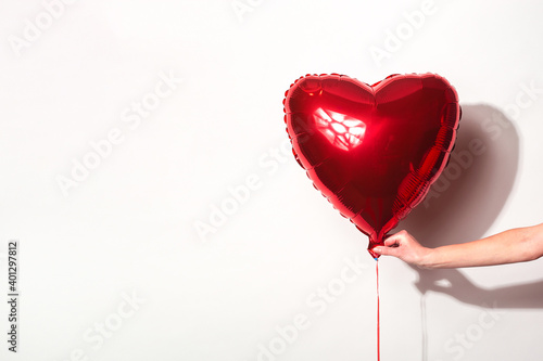 female hand holds a red air balloon in the form of a heart on a white background.