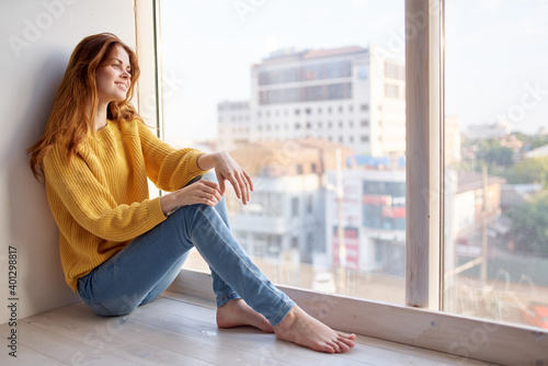 Woman on the windowsill in a yellow sweater and jeans leisure lifestyle