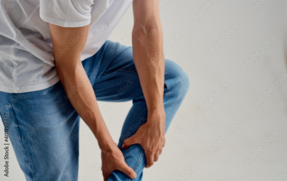 the guy touches his leg with his hands on a light background knee pain the guy touches his leg with his hands on a light background knee pain