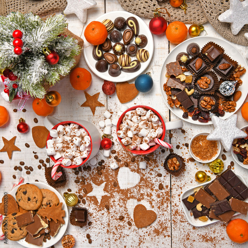 sweet food top view background for merry christmas or new year holiday decoration - chocolate candies, tangerines, cookies, marshmallow and cocoa latte on white wood