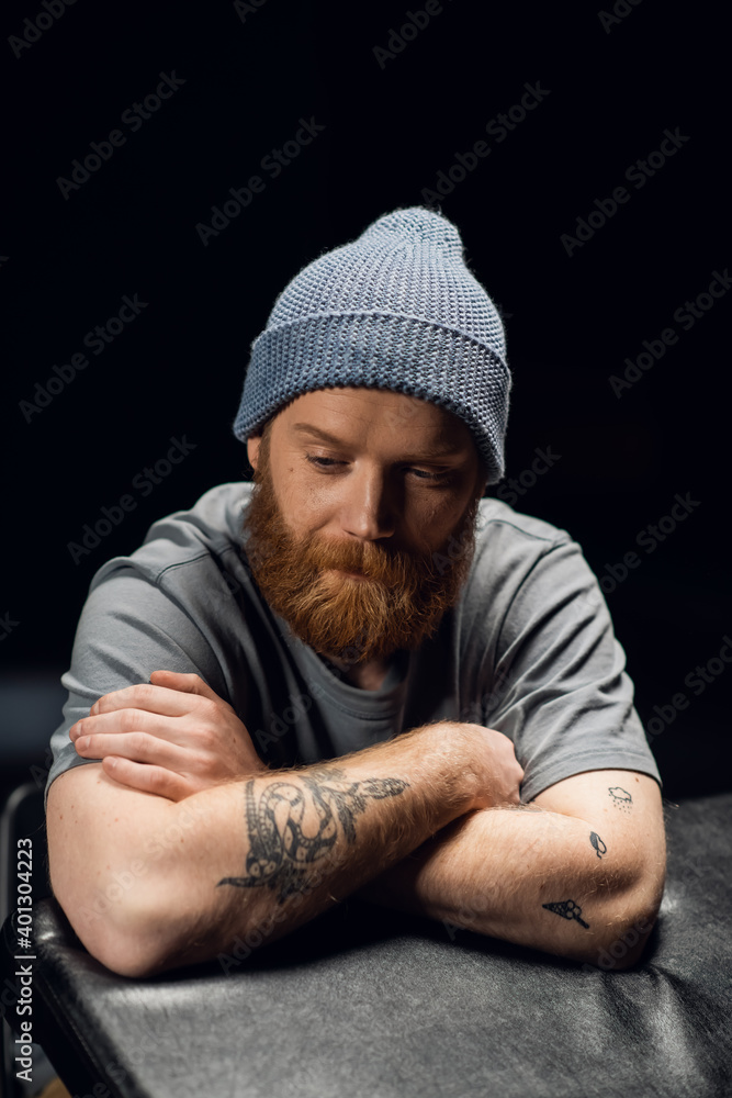 Portrait on a black background of a red-bearded tattooed scandinavian hipster man in a knitted hat Portrait on a black background of a red-bearded tattooed scandinavian hipster man in a knitted hat