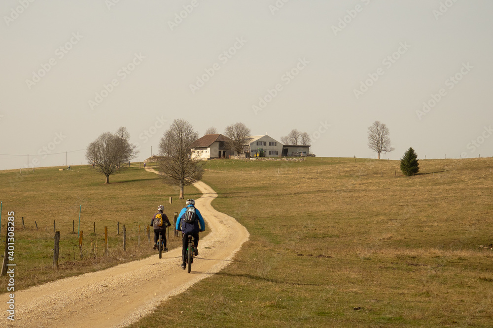 Obraz premium Two mountain bikers on a gravel road in front of a farm in the Swiss Jura hills
