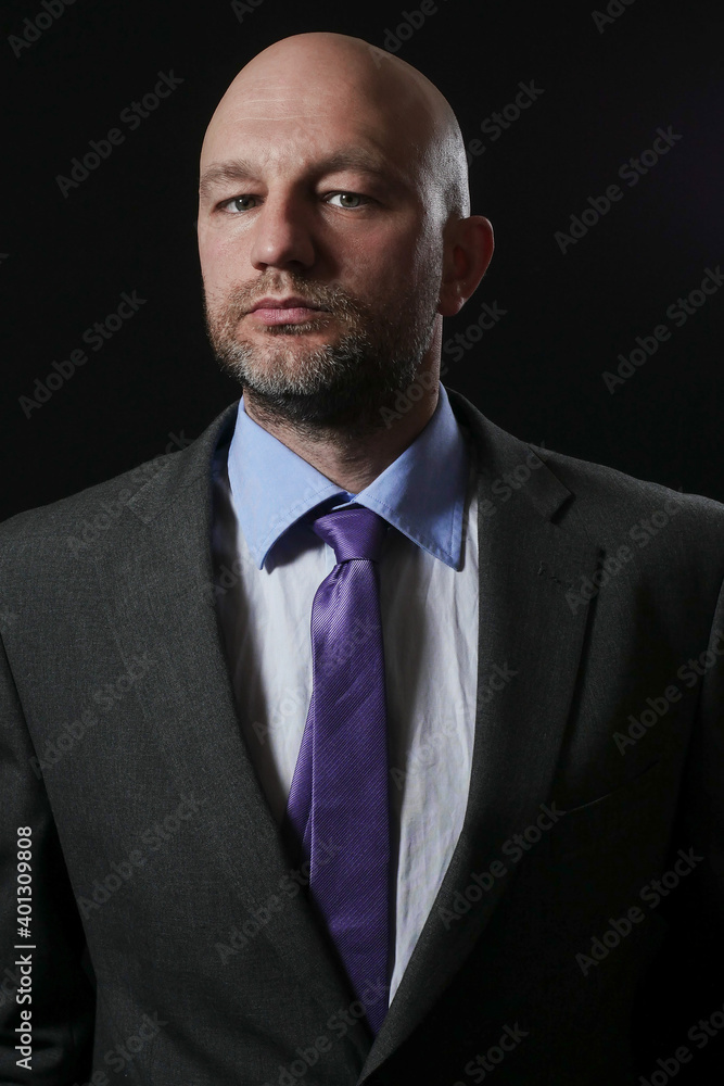 Portrait of a bold businessman with grey beard in his 40s on a dark background. The model dressed in grey suit, blue shirt and red tie. Concept boss, leader, professional Portrait of a bold businessman with grey beard in his 40s on a dark background. The model dressed in grey suit, blue shirt and red tie. Concept boss, leader, professional
