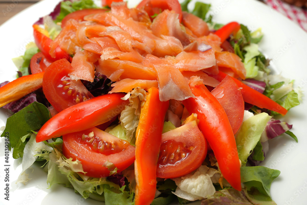 Serving of fresh salad with tomato, sweet pepper, lettuce and smoked salmon on a white plate. Healthy eating option. Serving of fresh salad with tomato, sweet pepper, lettuce and smoked salmon on a white plate. Healthy eating option.