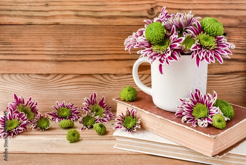 White mug with chrysanthemums, old books, wooden, rustic background. Concept for spring and summer.