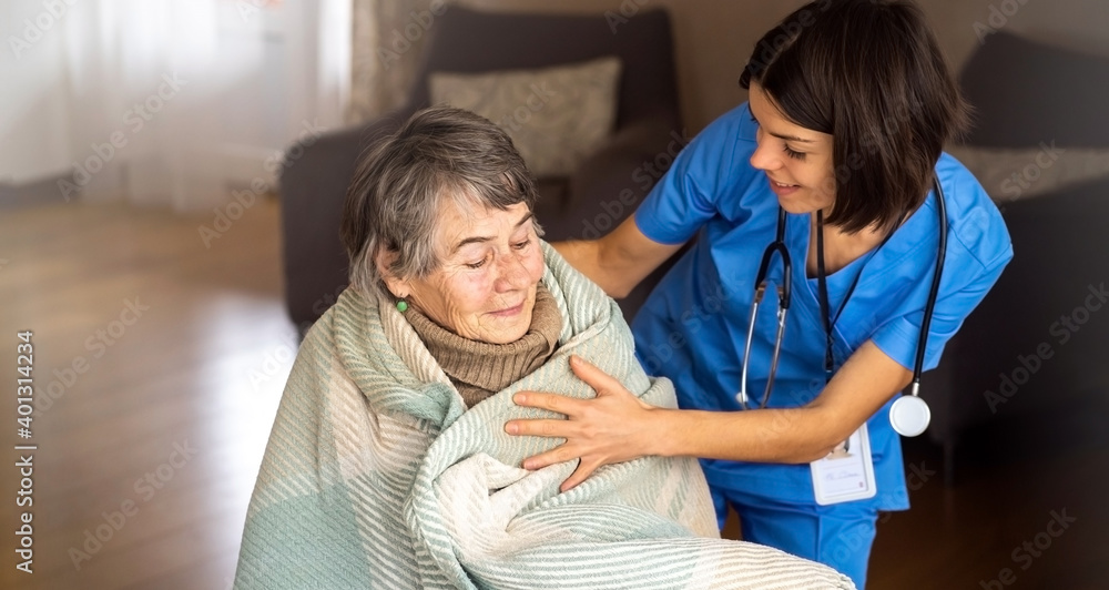 Obraz premium A young nurse takes care of an elderly 80-year-old woman at home, wraps a blanket around her. Happy retired woman and trust between doctor and patient. Medicine and healthcare.