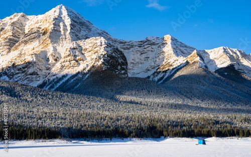 A blue ice fishing tent set up on the Spray Lakes of Peter Lougheed Provincial Park in the Canadian Rockies near Banff Alberta at sunrise.