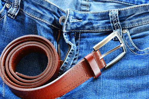 A close up image of an old reddish brown leather belt and a pair of faded blue jeans. 