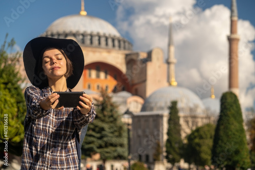 Photography A young pretty girl in a stylish hat and a plaid shirt poses, makes a selfie on the phone near to the Hagia Sophia mosque