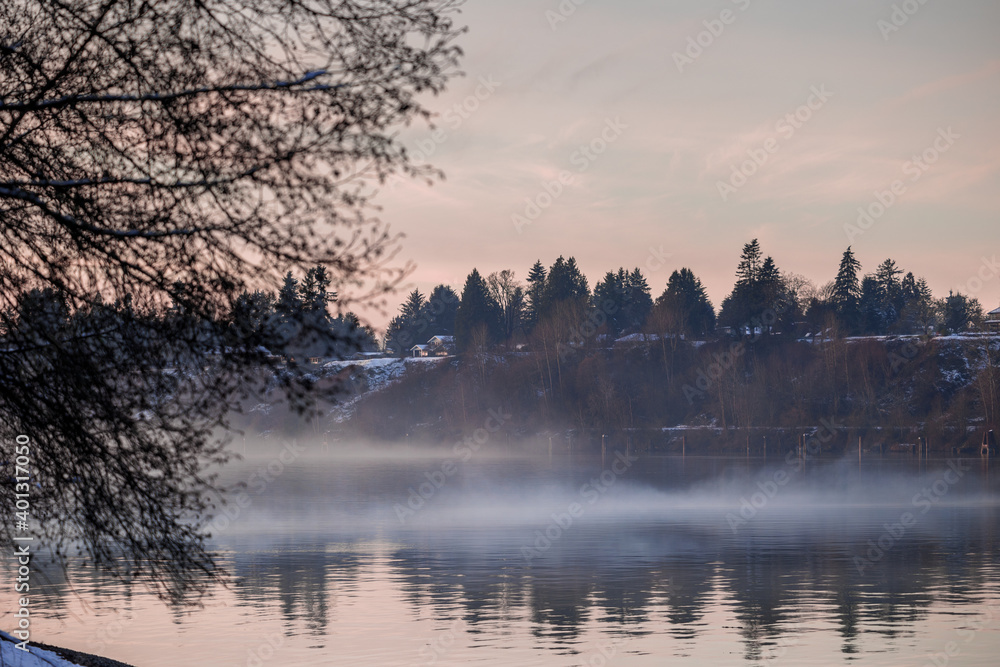 Fog sweeps over river during December sunset after snowfall