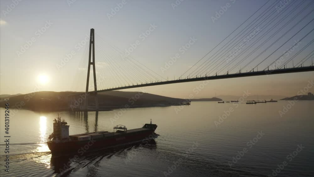 Aerial view of a big cargo ship with containers floating under the Russian Bridge in the morning. Russian island and other vessels are on the background. Russia Aerial view of a big cargo ship with containers floating under the Russian Bridge in the morning. Russian island and other vessels are on the background. Russia