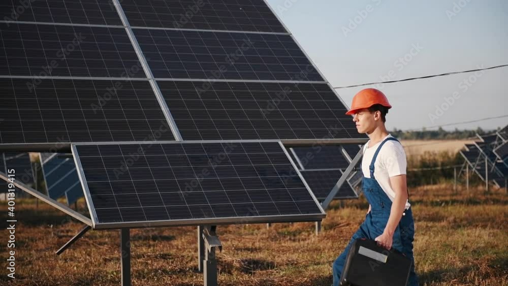 Repairman with tool case in hardhat and uniform is going near solar batteries. Repairman with tool case in hardhat and uniform is going near solar batteries.