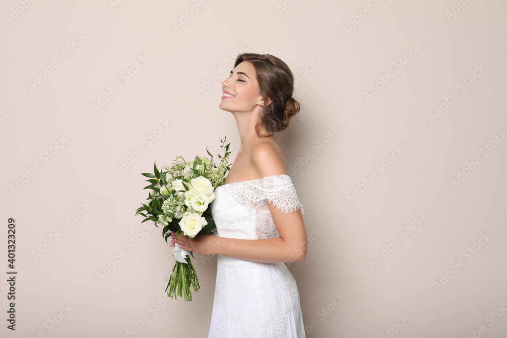 Young bride wearing wedding dress with beautiful bouquet on beige background