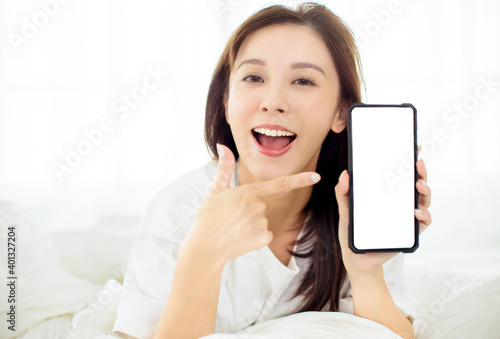 happy young woman showing smart phone while lying on the bed