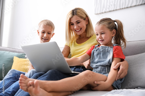 Happy mother using laptop with her children on sofa at home © New Africa