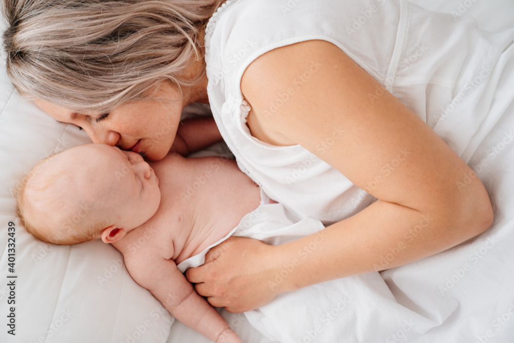 mom is mom is lying down with a baby in a white bed after feeding breast milk. mom is mom is lying down with a baby in a white bed after feeding breast milk.