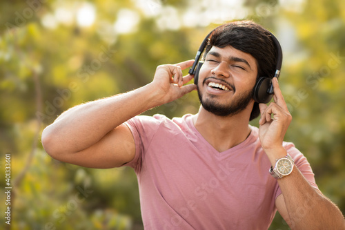 Young man enjoying music in headphone on nature background.