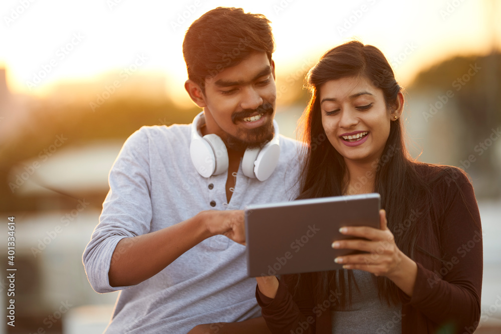 Happy young friends using tablet with headphones at outdoor. Happy young friends using tablet with headphones at outdoor.