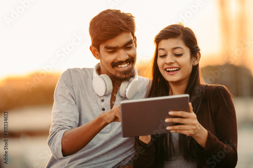 Photography Happy young friends using tablet with headphones at outdoor.
