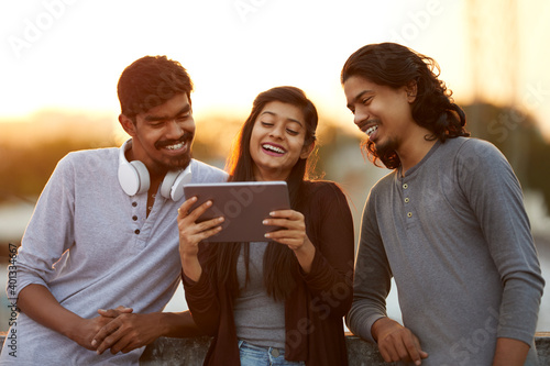 Cheerful young friends playing in digital tablet on terrace at outdoor. photo