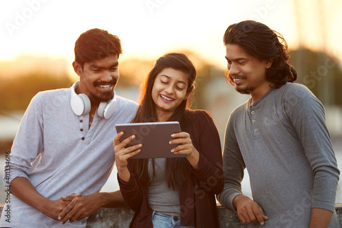 Cheerful young friends playing in digital tablet on terrace at outdoor. photo