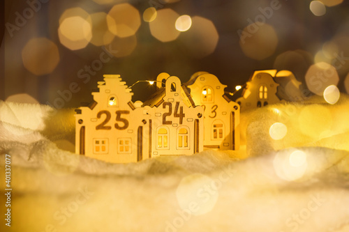 Wooden house toy with number 24 and light on on dark background with yellow bokeh. The concept of the advent calendar for Christmas. Eco decorations for home interior.