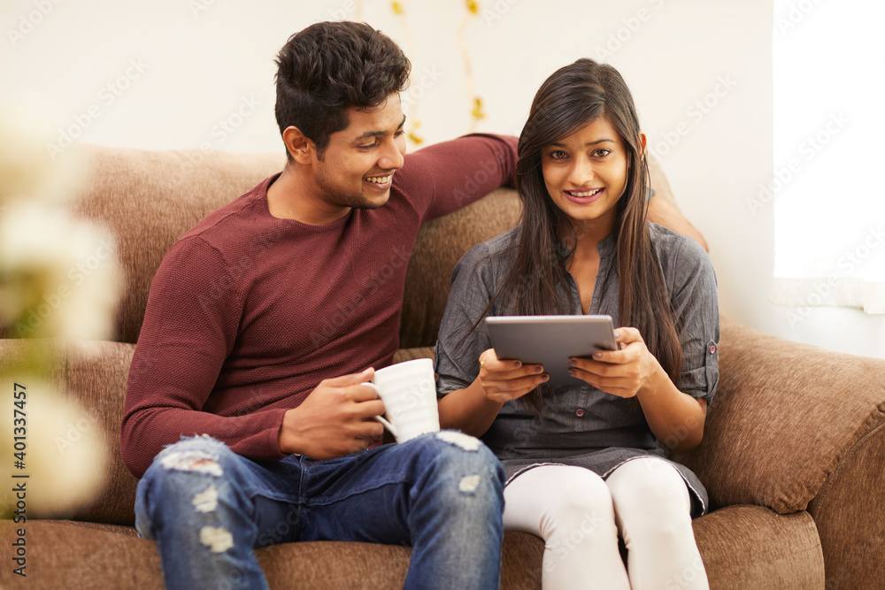 Cheerful young beautiful couple chatting with tablet and coffee on sofa at home. Cheerful young beautiful couple chatting with tablet and coffee on sofa at home.