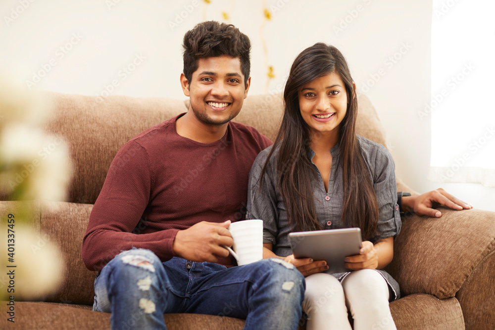 Cheerful young beautiful couple chatting with tablet and coffee on sofa at home. Cheerful young beautiful couple chatting with tablet and coffee on sofa at home.