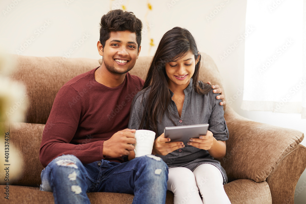 Cheerful young beautiful couple chatting with tablet and coffee on sofa at home. Cheerful young beautiful couple chatting with tablet and coffee on sofa at home.