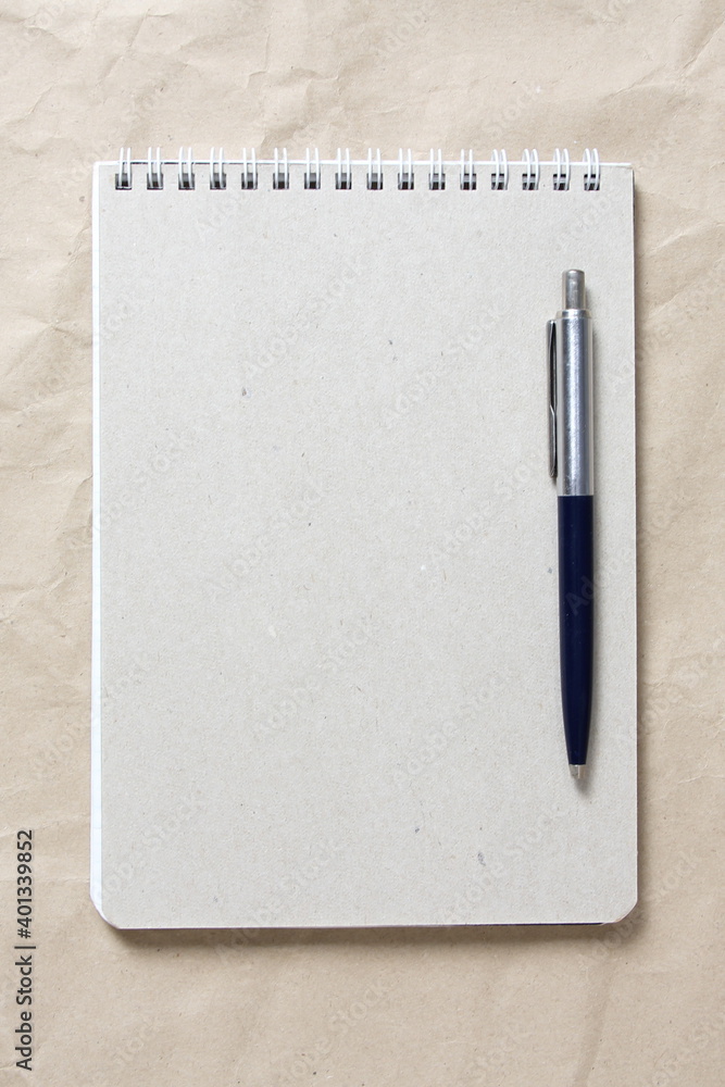 Gray notepad with white coiled spring and pen on a background of beige crumpled craft paper Gray notepad with white coiled spring and pen on a background of beige crumpled craft paper