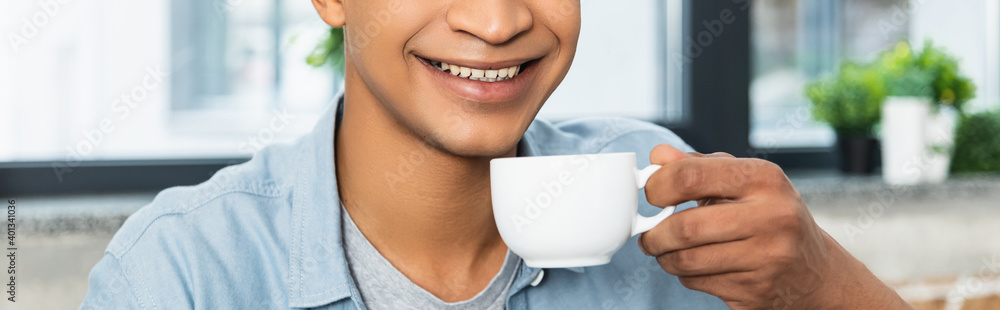 cropped view of young african american man holding cup of coffee, banner. - obrazy, fototapety, plakaty 