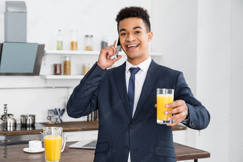 happy african american businessman holding glass of orange juice and talking on smartphone. happy african american businessman holding glass of orange juice and talking on smartphone.