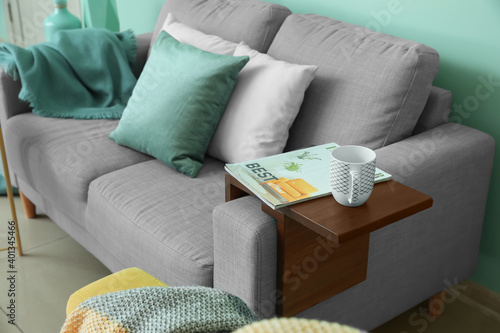 Cup of tea and magazine on armrest table in room