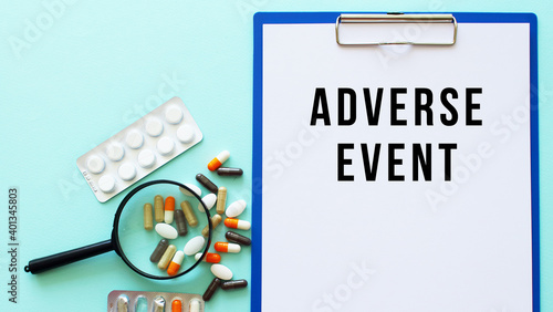 A clipboard with paper lies on a table near drugs and a syringe. Inscription ADVERSE EVENT.
