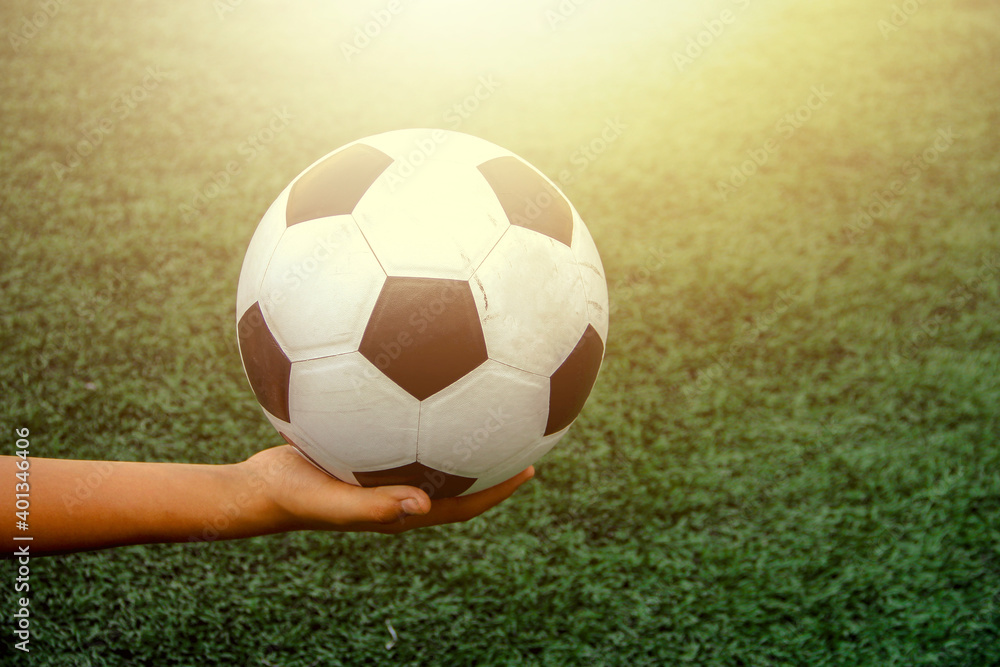 The child's hand is holding an old black and white soccer ball