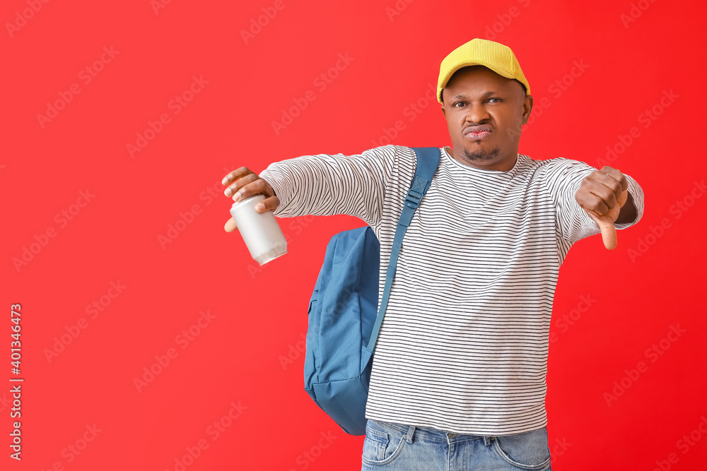 Displeased African-American man with soda showing thumb-down on color background