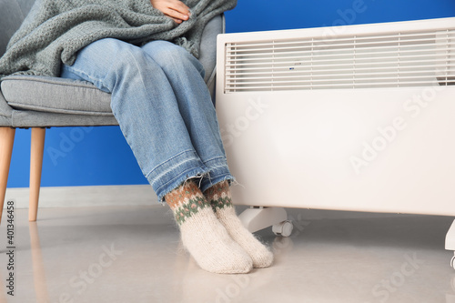 Mature woman near electric heater at home. Concept of heating season © Pixel-Shot