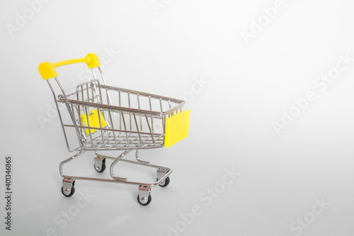 Grocery cart with yellow handle on a gray background. Side view. Horizontal format. Copyspace © Maria Sannikova