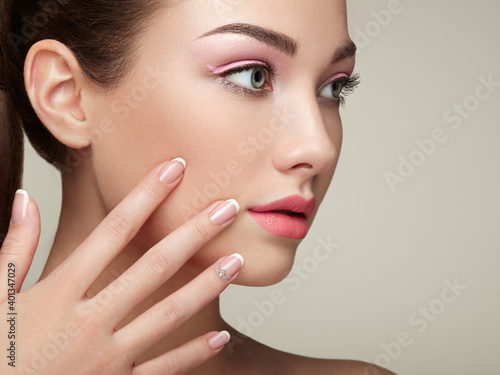 Beauty brunette woman with perfect makeup. Pink lips and nails. Perfect eyebrows. Skin care foundation. Beauty girls face isolated on beige background. Hands with beautiful elegant manicure