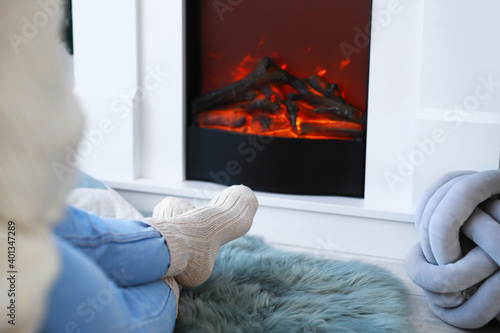 Young woman sitting near electric fireplace at home. Concept of heating season